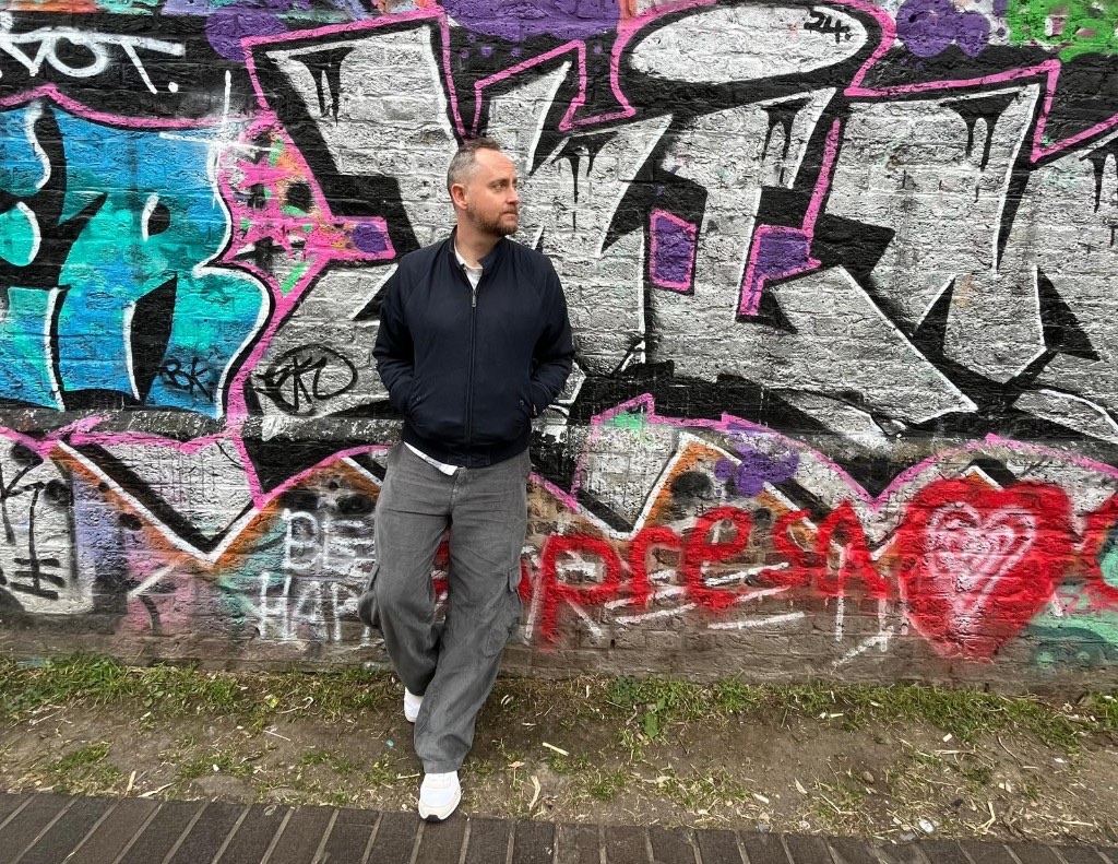 Paul Wheatcroft leaning against a graffiti-covered brick wall